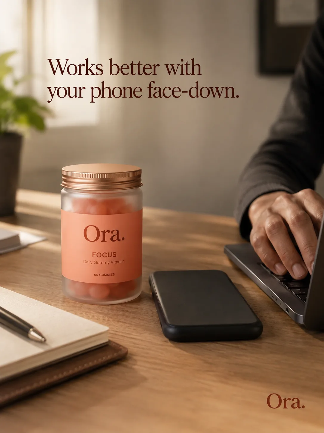 Ora — jar, face-down phone, hand on a keyboard mid-work, 'Works better with your phone face-down.'