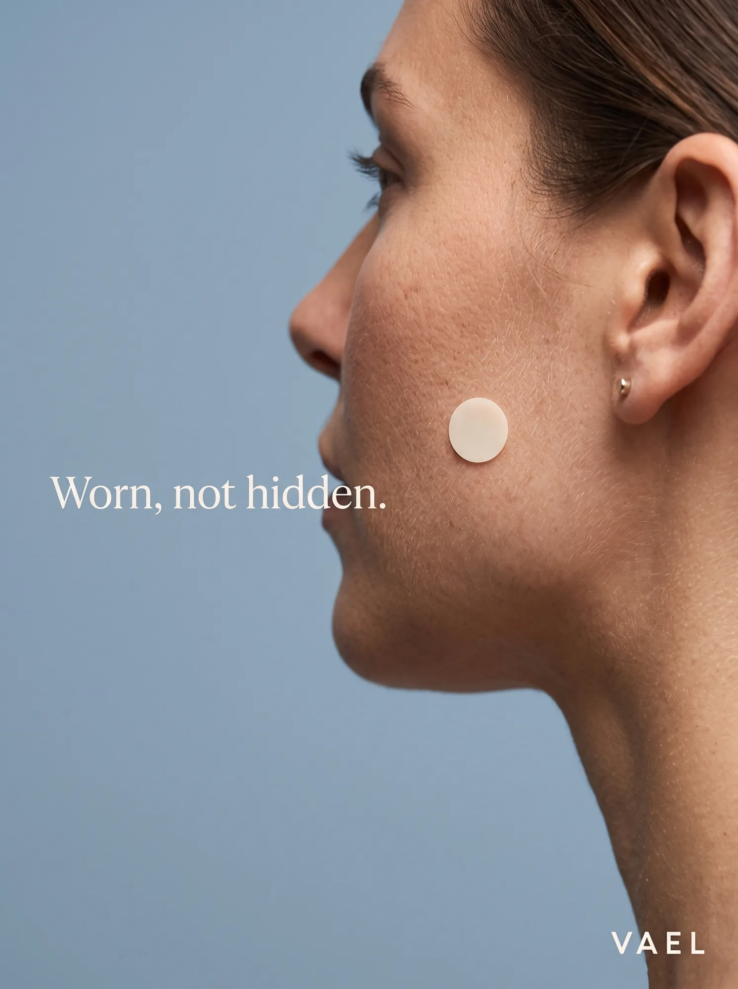 Vael — beauty-campaign profile crop, one patch treated like a stud earring, 'Worn, not hidden.'